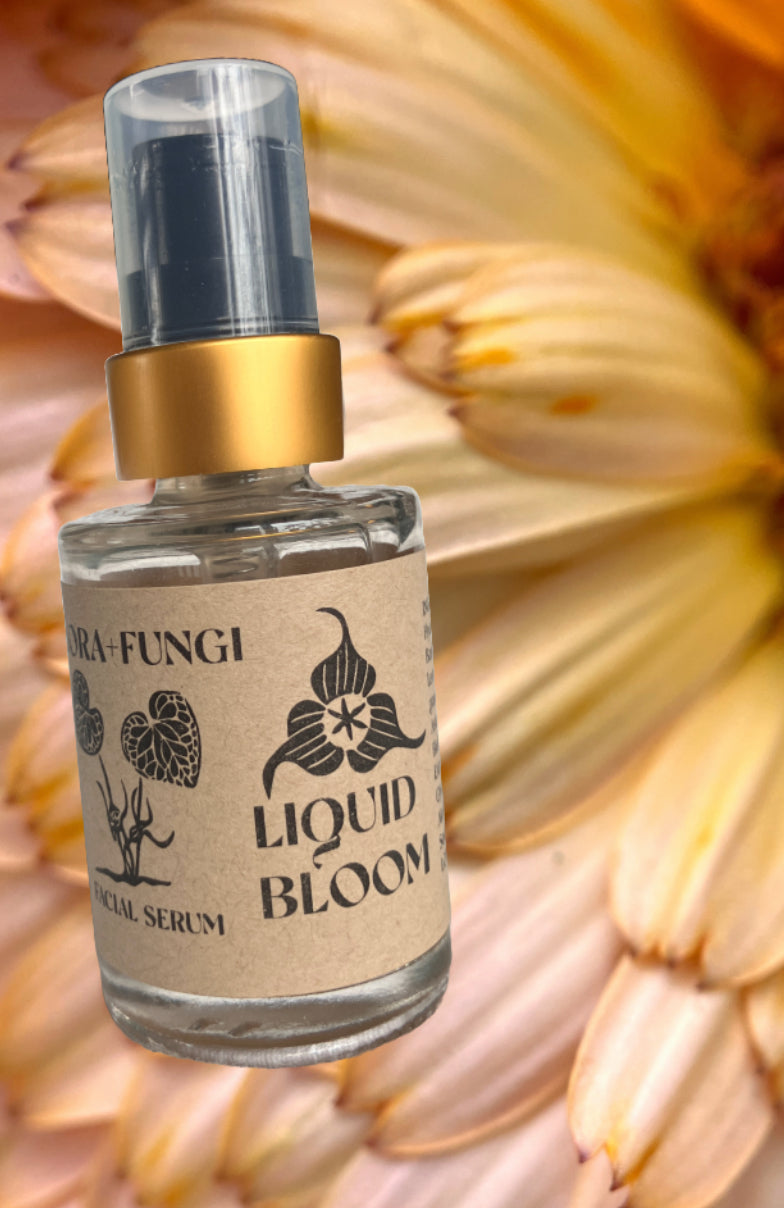 Bottle of 'Liquid Bloom' serum with a gold cap on a textured beige background