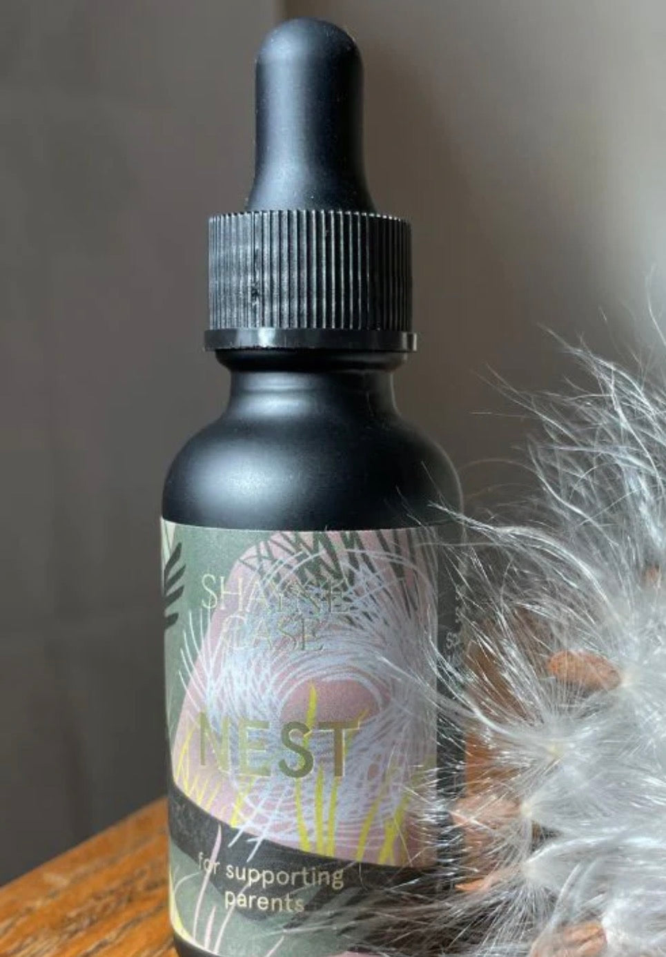 Black bottle with dropper labeled 'Nest' on a wooden surface with a blurred background