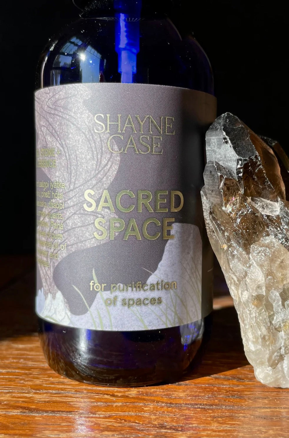 Bottle labeled 'Shayne Case Sacred Space' with a crystal on a wooden surface