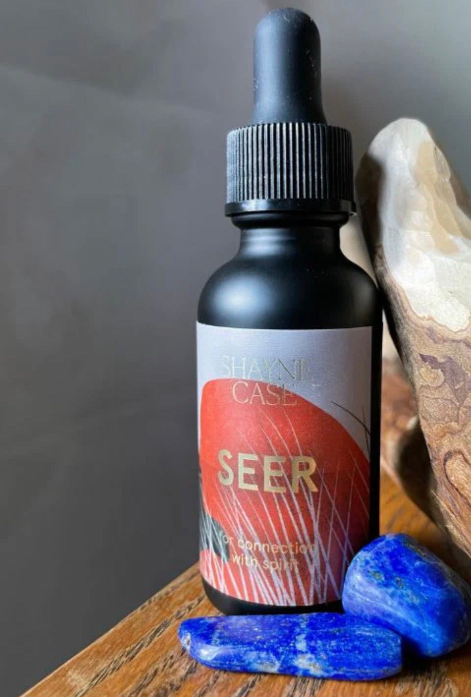 Bottle labeled 'SEER' with a dropper on a wooden surface with blue stones and a stone background.