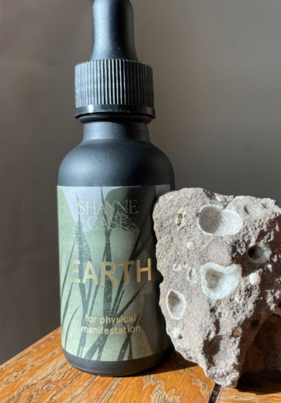 Bottle labeled 'Earth' by Shayne Case with a dropper next to a piece of rock on a wooden surface.