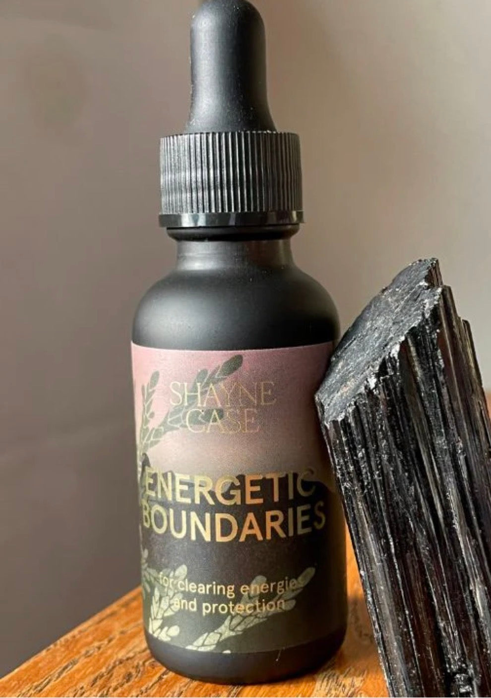 Bottle labeled 'Energetic Boundaries' by Shayne Case with a crystal on a wooden surface.