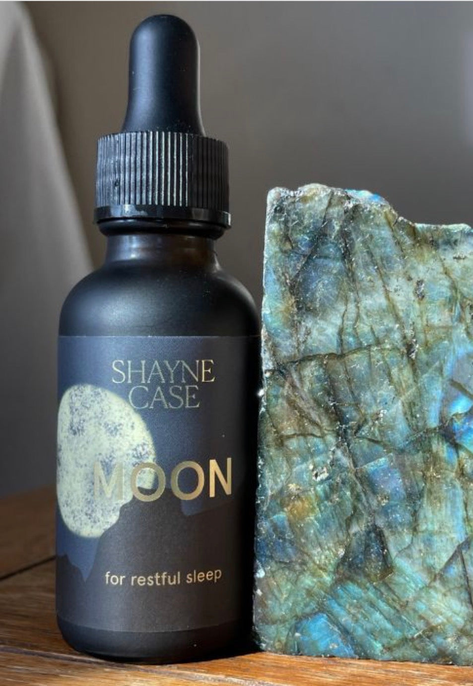 Bottle of Shaye Case Moon essence next to a crystal on a wooden surface
