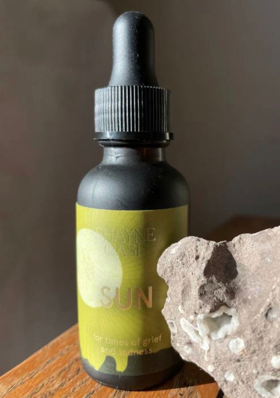 Bottle labeled 'Sun' by Shayne Case on a wooden surface with a stone background